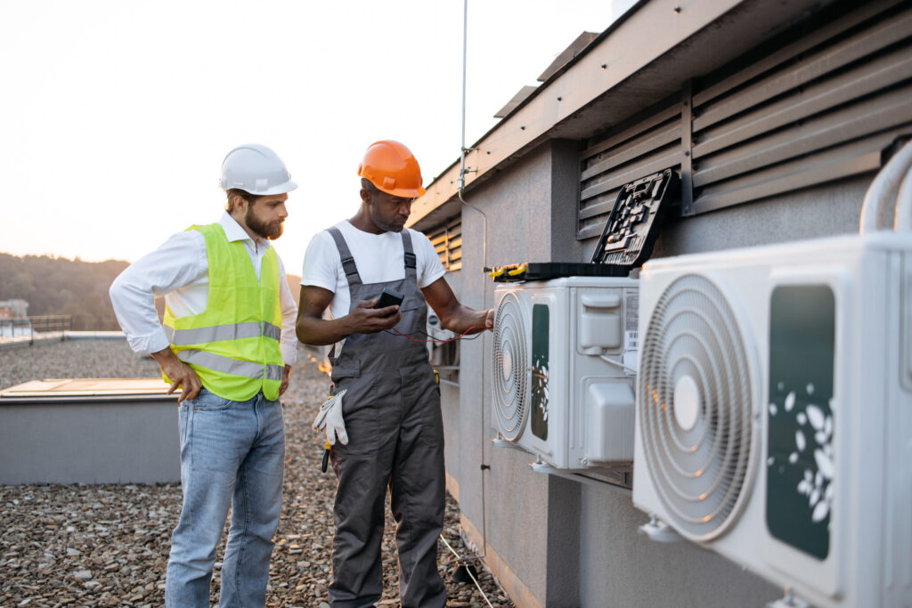 Repairmen with multimeter fixing air conditioner on rooftop